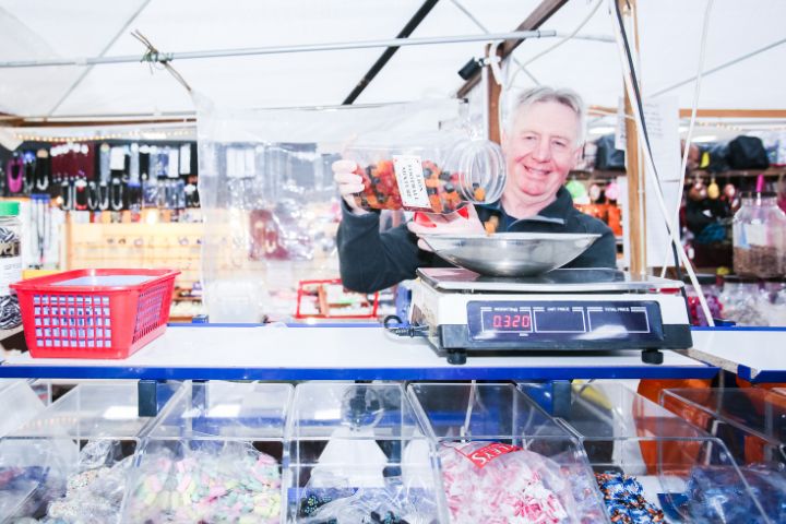 A smiling man weighing out sweets from a plastic jar onto some weighing scales