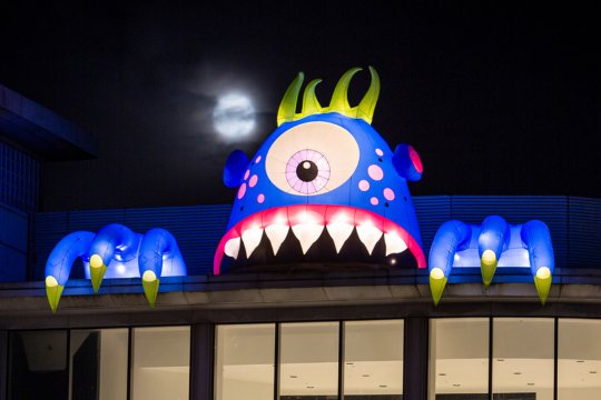 Large blue inflatable cyclops with claws devouring the top of a building