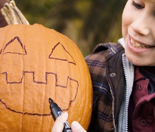 Young boy drawing a scary face on a pumpkin