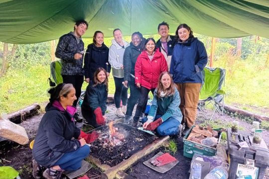 Group of people standing around a camp fire.