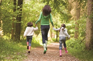 A woman and 2 children skipping down a woodland lane.